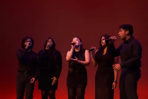 Event photo for the Multicultural Student Center: five singers with microphones on a red-lit stage at MCOR.