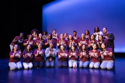 Event photo for the Multicultural Student Center: a large group in maroon shirts posing on stage at MCOR.