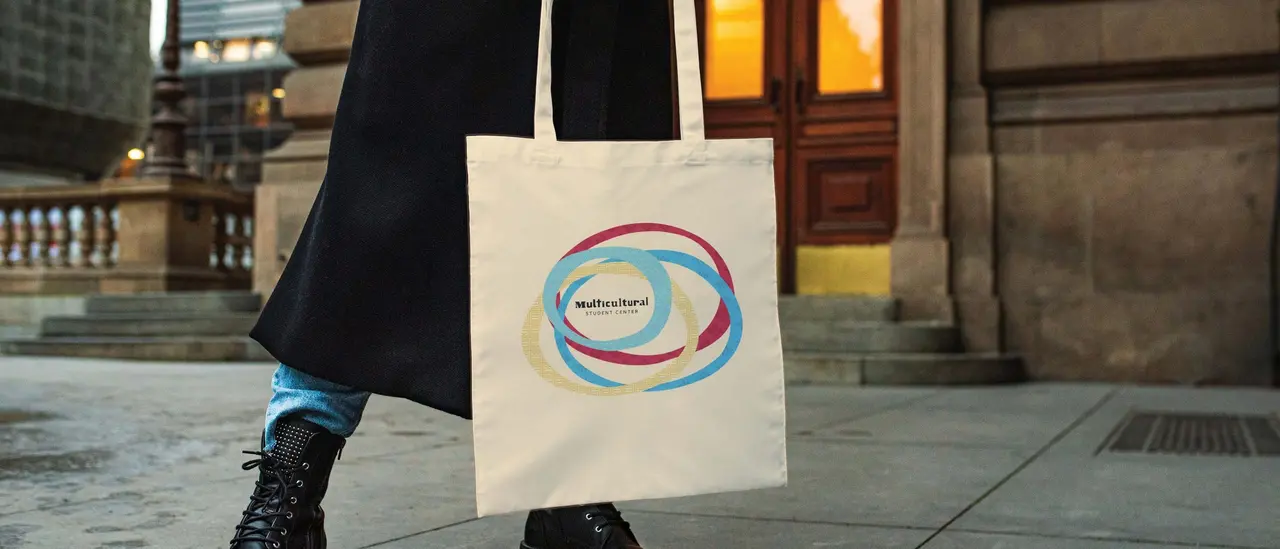 Team merchandise for the Multicultural Student Center: a canvas tote with the four-circle graphic, carried on a city street.