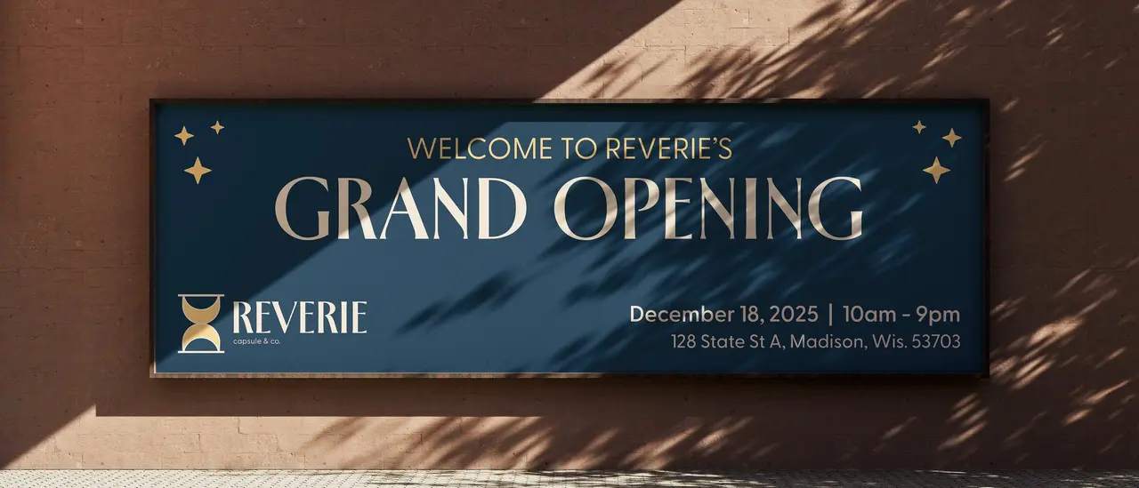 Billboard for Reverie Capsule & Co.: “Welcome to Reverie’s Grand Opening” on a sunlit clay wall.